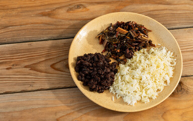 Refried black beans (frijoles refritos), basmati rice, and a braised swiss chard - a homemade, tasty vegan meal. Rustic wooden table with copy space. 