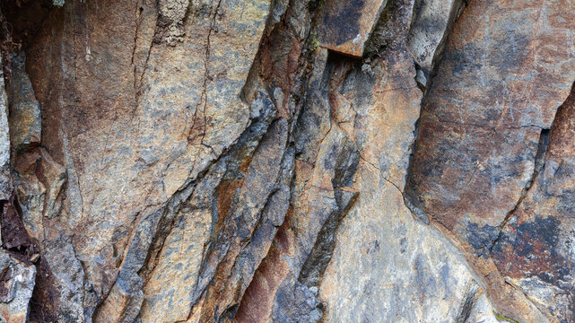 Coarse stone wall with layered mineral tones, natural cracks and shades of brown and gray create an organic rocky texture ideal for abstract backgrounds