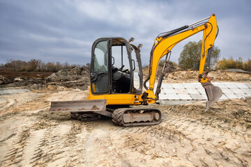 A yellow excavator is positioned on a construction site, preparing to dig into the sandy ground...