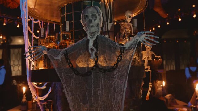 Bar counter lavishly decorated for halloween with hanging skeletons, white cobwebs, illuminated bottles and chains creating a spooky, festive nightclub atmosphere for guests