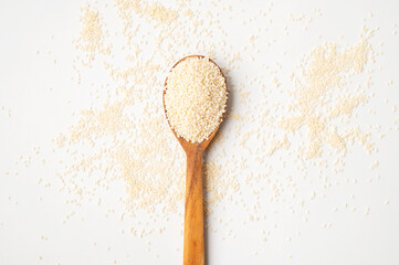 Close-up of white sesame seeds in wooden spoon with green leaves on light white background. Healthy organic seeds, cooking ingredient. Sesamum indicum. Top view flat lay