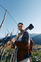 Fototapeta premium Woman with axe outdoors in mountains rural fence tool nature, holding wooden handle by vineyard posts. Portrait of a young serious worker in rustic landscape with sunlight and determination.