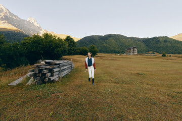 Fototapeta premium Woman walking across a wide meadow and open field with distant mountains in the background, nature landscape in a rural setting, casual outfit with boots and jacket for outdoor exploration.