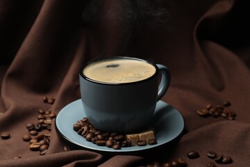 Aromatic coffee in cup, beans and brown sugar on fabric, closeup