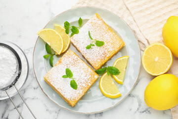 Tasty lemon bars with powdered sugar, mint and fresh fruits on white marble table, flat lay