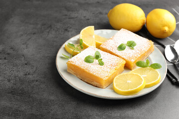 Tasty lemon bars with powdered sugar, mint and fresh fruits on grey table, closeup. Space for text
