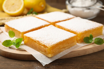 Tasty lemon bars with powdered sugar and mint on wooden table, closeup