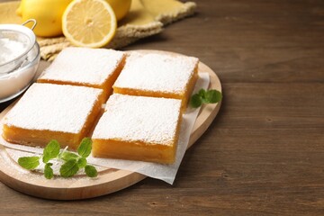 Tasty lemon bars with powdered sugar and mint on wooden table, closeup. Space for text
