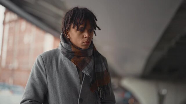 African american man waiting someone under bridge, medium portrait in winter. Trendy young townsman in urban landscape, cold weather in city in autumn, meeting on city street, feel cold and boring