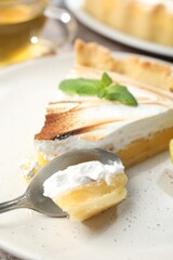 Slice of tasty lemon meringue tart with mint served on table, closeup