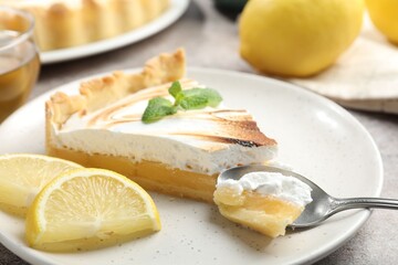 Slice of tasty lemon meringue tart with mint served on light grey table, closeup
