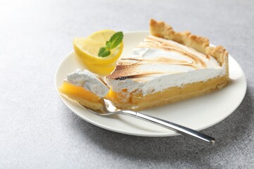 Slice of tasty lemon meringue tart with mint served on light grey table, closeup