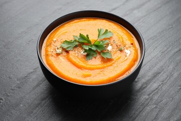 Tasty pumpkin cream soup with parsley in bowl on grey table, closeup