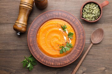 Tasty pumpkin cream soup in bowl served on wooden table, flat lay