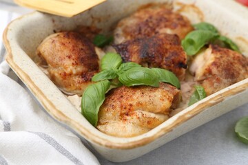 Tasty cooked chicken thighs with basil in baking dish on light grey table, closeup