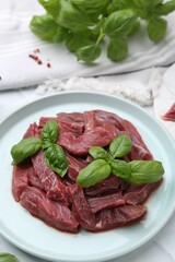Pieces of raw beef meat and basil on table, closeup