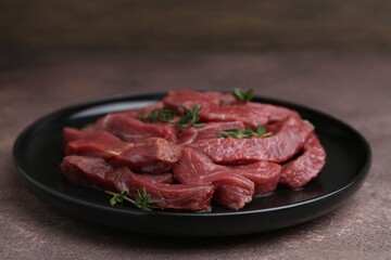 Pieces of raw beef meat and thyme on brown table, closeup
