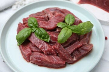 Pieces of raw beef meat and basil on table, closeup