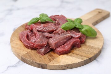Pieces of raw beef meat and basil on white marble table, closeup