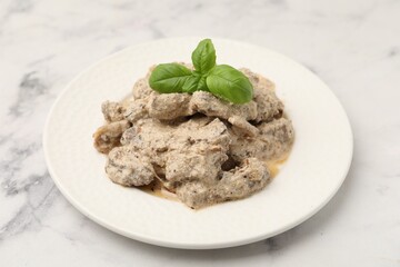 Tasty beef Stroganoff with basil on white marble table, closeup