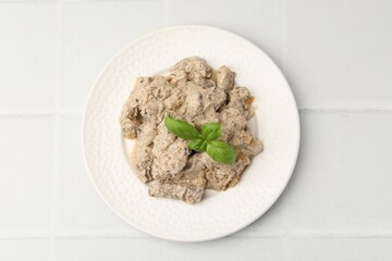 Tasty beef Stroganoff with basil on white tiled table, top view