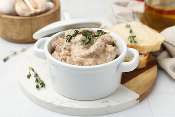 Tasty beef Stroganoff with thyme in casserole, bread and spices on white tiled table, closeup