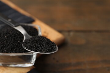 Aromatic black caraway in glass bowl and spoon on wooden table, closeup. Space for text