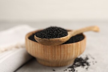 Aromatic black caraway in wooden bowl and spoon on light grey table, closeup