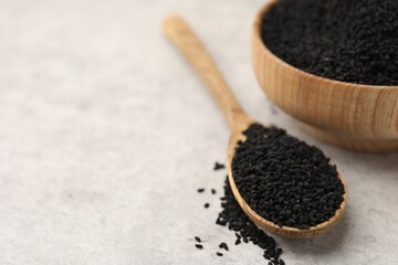 Aromatic black caraway in wooden spoon and bowl on light grey table, closeup. Space for text