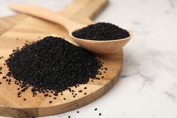 Aromatic black caraway in wooden spoon on white marble table, closeup. Space for text