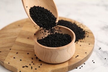 Pouring aromatic black caraway into bowl at white marble table, closeup