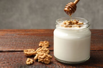 Dripping honey into Greek yogurt with walnuts at wooden table, closeup. Space for text