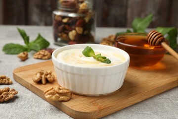 Delicious Greek yogurt with honey, nuts and mint on light grey table, closeup