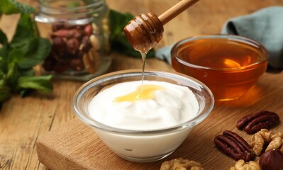 Dripping honey into Greek yogurt and nuts on wooden table, closeup
