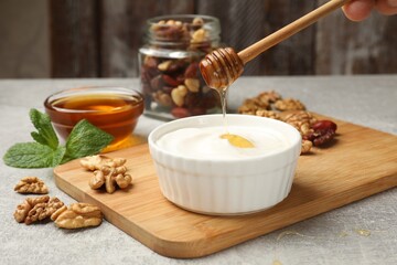 Woman dripping honey into Greek yogurt and walnuts on grey table, closeup