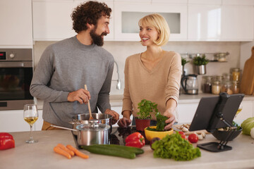 In a bright and inviting kitchen, a couple laughs while preparing a meal together. Fresh vegetables surround them as they work on a delicious recipe.