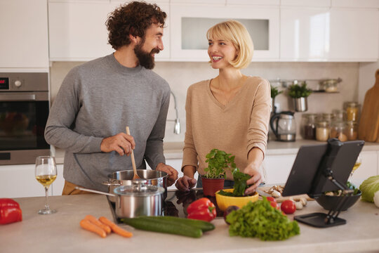 In a bright and inviting kitchen, a couple laughs while preparing a meal together. Fresh vegetables surround them as they work on a delicious recipe.