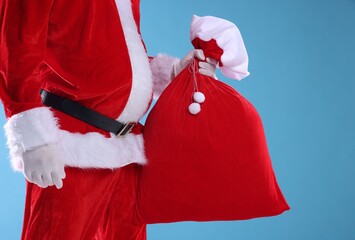 Santa Claus holding sack on light blue background, closeup. Merry Christmas and Happy New Year