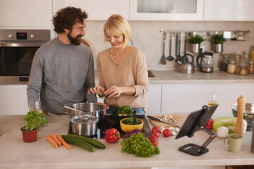 A man and woman are cooking in a stylish kitchen. They are chopping greens and mixing colorful vegetables in pots, sharing smiles and enjoying their time together.
