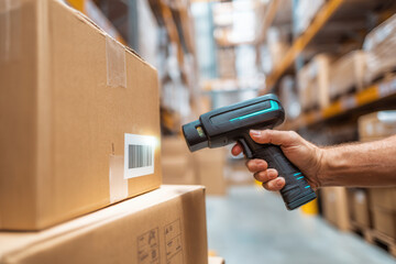 Hand holding barcode scanner in a warehouse while scanning packages for inventory control