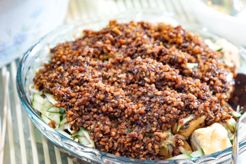 Close-up of Rojak Tauhu, a traditional Malaysian tofu salad with fresh vegetables and savory dark sauce in a glass bowl on a striped surface.