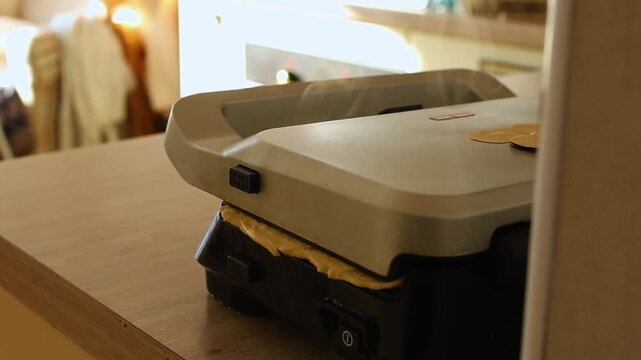 Close-up of a modern electric indoor grill (panini or waffle maker) closed and releasing hot steam/vapor on a kitchen counter. Focuses on homemade cooking, food preparation, and breakfast.
