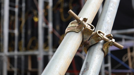 Swivel clamp holds a steel pipe. Pipe clamps and metal scaffolding parts for supporting an outdoor concert stage structure with selective focus.