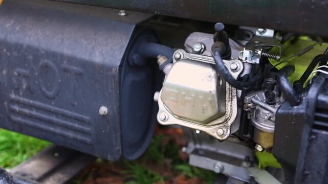 Extreme close-up of a dirty gasoline generator engine block. The carburetor is actively working, and the machine is vibrating as it runs, supplying emergency power.