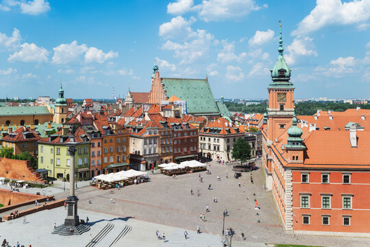 A sunny view of Warsaw’s Castle Square with colorful historic buildings, a central column monument, cafés, and people enjoying the lively square under a blue sky.