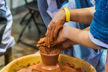 Hands shaping clay on pottery wheel