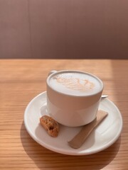 Cappuccino white cup coffee on table in cozy cafe with morning light, warm atmosphere, latte foam art, relaxing environment, inviting drink, ceramic mug, peaceful moment, coffee break, enjoying aroma 
