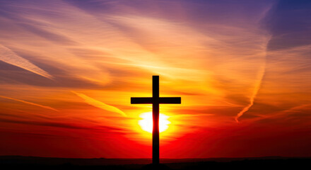Silhouette of a Christian cross standing against a dramatic and colorful sunset sky with vibrant orange and red hues.