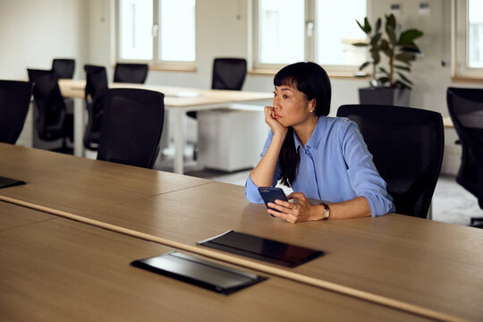 Asian Woman In Blue Shirt At Modern Office Conference Table Using Smartphone During A Meeting - Powered by Adobe
