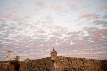 Historic coastal fort with distant tower under dusk clouds